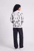 A model shown from the back wearing a white hemp bomber jacket with a black abstract eco-print, paired with black pants and white sneakers, against a light gray studio background.