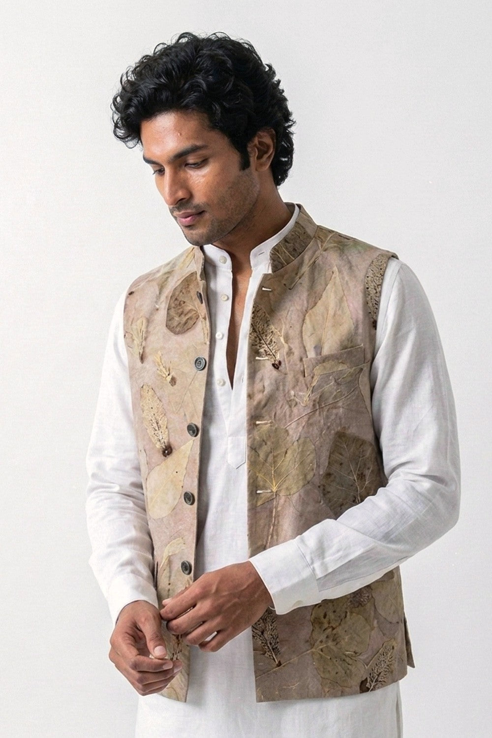 A man wearing a white kurta and a beige eco-printed hemp vest with brown leaf patterns, photographed against a plain light background.