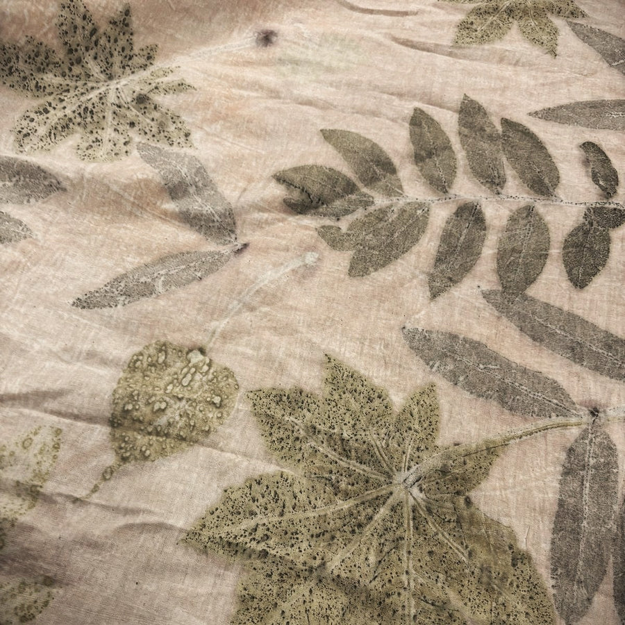 A close-up of a textured hemp fabric featuring a botanical leaf pattern in muted olive green and gray on a warm beige background.
