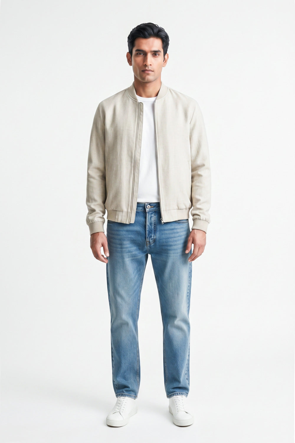 A man modeling a light beige linen bomber jacket over a white t-shirt and blue jeans, standing against a plain white studio background.