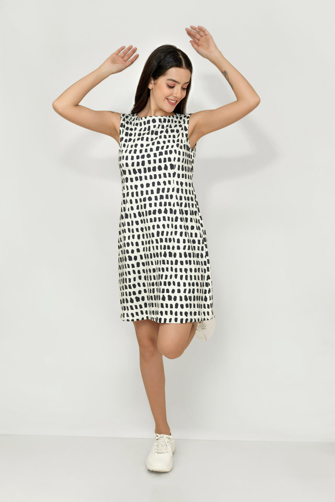 A woman wearing a sleeveless, knee-length black and white hemp dress with a boat neckline, standing before white background