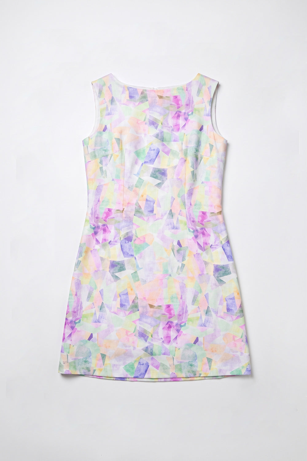 A woman modeling a sleeveless A-line  dress with an abstract pastel watercolor pattern in purple, pink, green, and blue on a white base, paired with white sneakers, against a plain white studio background.