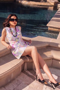 A woman wearing a pastel tie-dye mini hemp dress, black sunglasses, and black high heels sits on the stone steps next to a swimming pool.