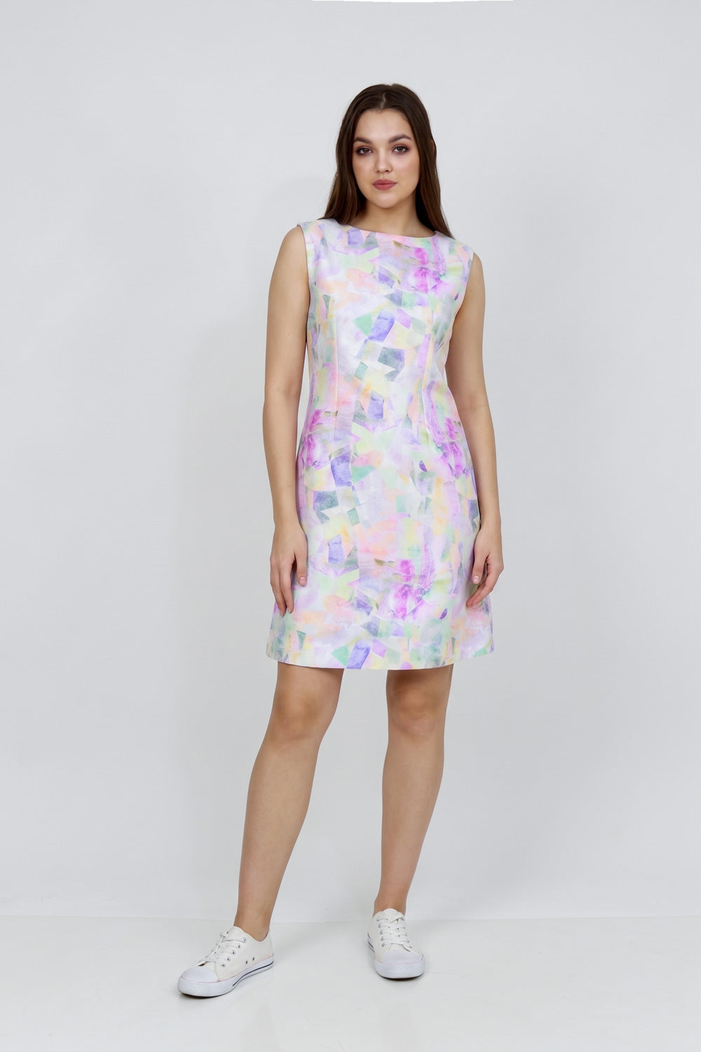A woman modeling a sleeveless knee-length hemp dress with a pastel multicolor abstract print, paired with white sneakers, against a plain light gray studio background.