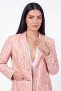 A woman modeling a pink linen blazer with a white paisley pattern over a white V-neck top, photographed against a plain white studio background.