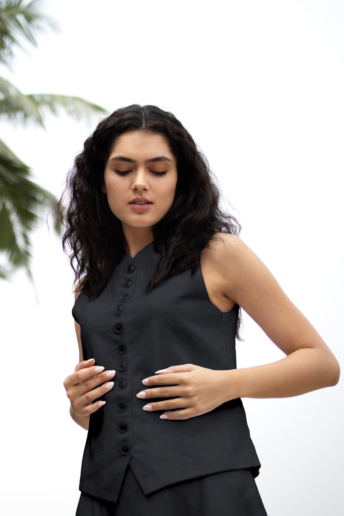 Woman wearing a black sleeveless top with buttons against a white background