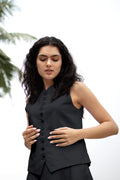Woman wearing a black sleeveless top with buttons against a white background