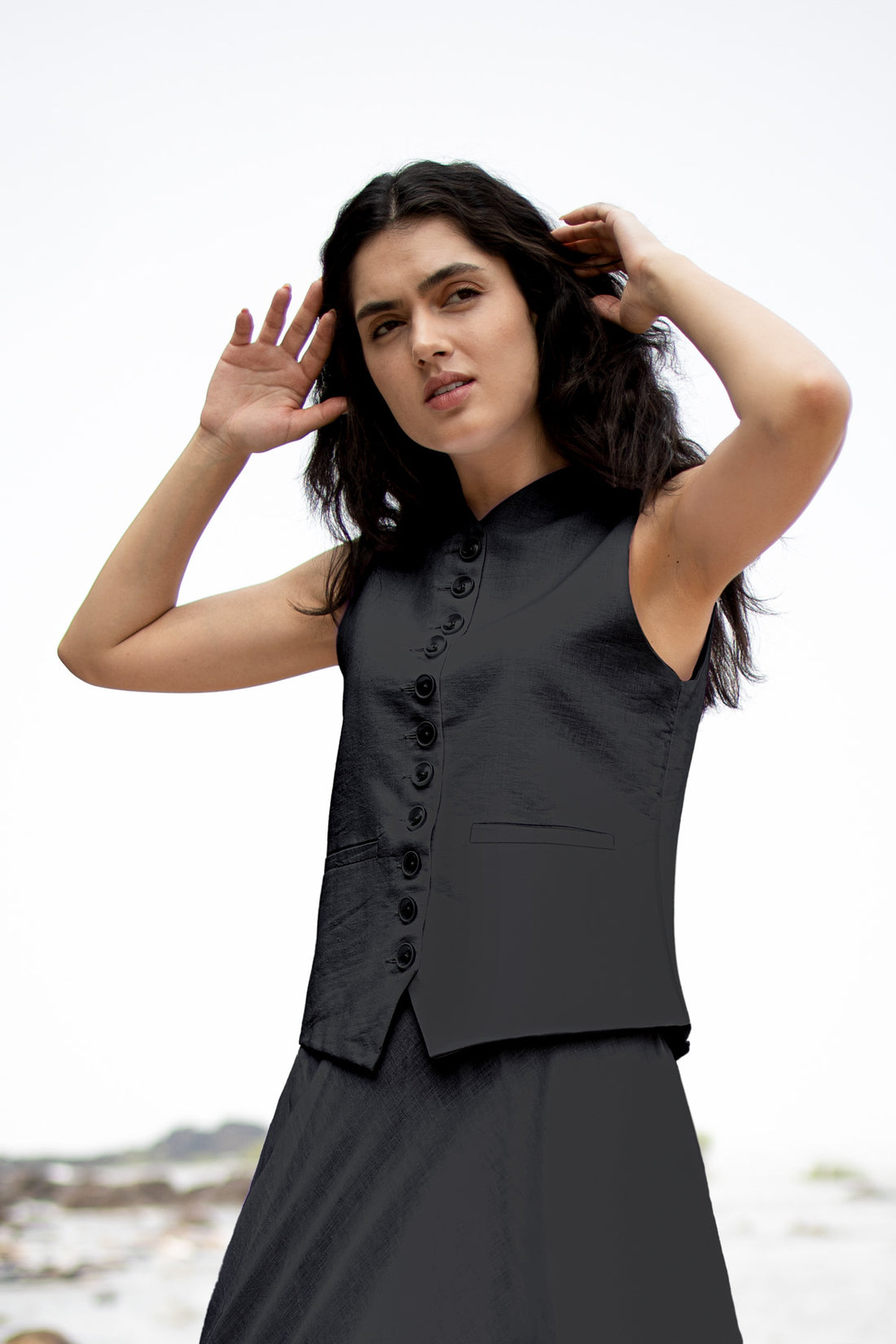 Woman wearing a black sleeveless top with buttons against a white background