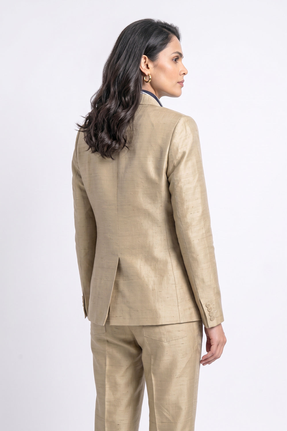 A woman shown from the back wearing a tailored beige silk suit with a textured fabric, photographed against a clean white studio background.
