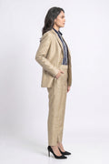 A woman stands in profile wearing a tailored beige suit with a silk blazer and matching trousers, layered over a navy and white striped shirt, and paired with black high heels against a light gray studio background.