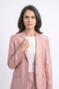 A woman modeling a light pink textured silk blazer and matching trousers over a white top, photographed against a plain light gray studio background.