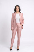 A woman modeling a dusty pink tailored suit set consisting of a silk blazer and matching trousers, styled with a white top and black heels against a light gray studio background.