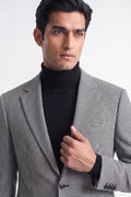 A man wearing a black and white checks cotton blazer over a black turtleneck sweater, photographed against a clean light gray studio background.