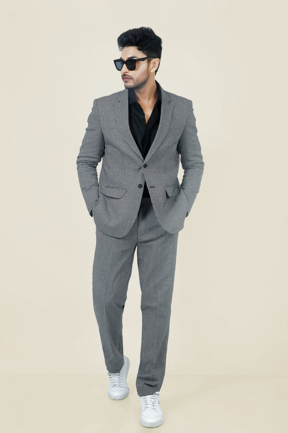 Stylish man in a gray and white checkered cotton jacket and pants, with a black shirt and white sneakers.