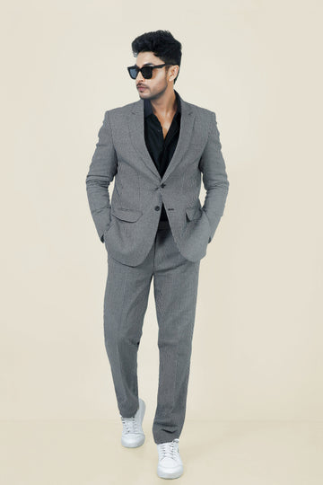 Stylish man in a gray and white checkered cotton jacket and pants, with a black shirt and white sneakers.