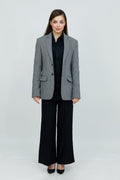 A woman wearing a gray and white patterned cotton blazer, a black button-down shirt, and black wide-leg trousers.