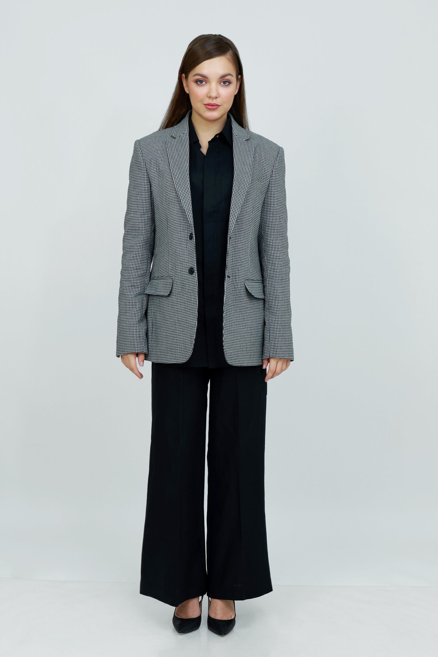 A woman wearing a gray and white patterned cotton blazer, a black button-down shirt, and black wide-leg trousers.