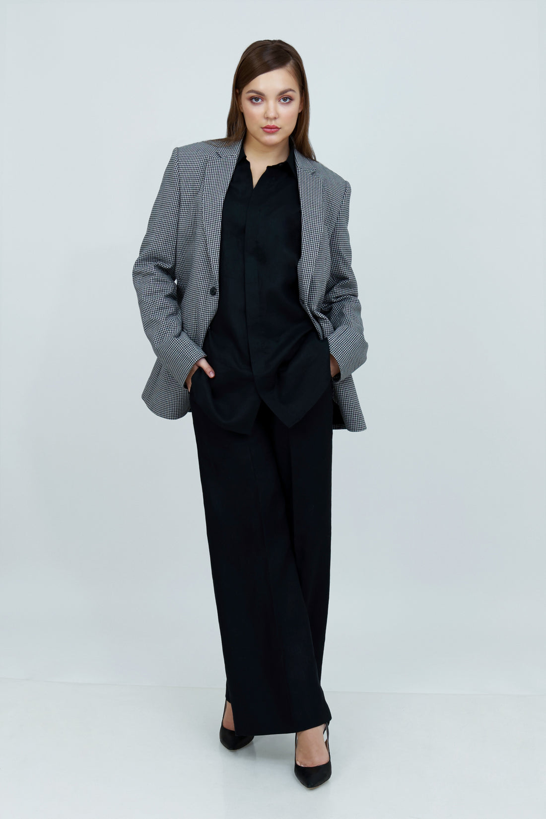 A person wearing a single-breasted, gray, checkered unisex cotton jacket with a notch lapel and functional sleeves, paired with a black outfit.