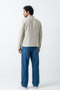 A man is shown from the back wearing a light beige linen jacket and blue jeans against a plain white studio background.