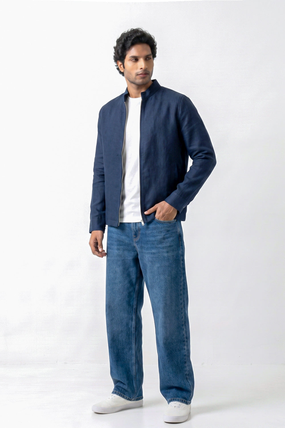 A man modeling a dark navy blue zip-up linen jacket over a white t-shirt and blue jeans, standing against a plain white studio background.