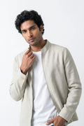 A man wearing a light beige linen-jacket over a white t-shirt, posing against a plain white studio background.