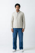 A man wearing a light beige linen jacket with a stand collar and front zipper, paired with blue jeans and white sneakers, standing against a white studio background.