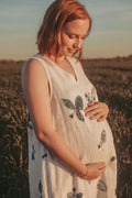 Pregnant woman wearing a hemp eco-printed dress with natural botanical leaf and flower motifs, sustainable fashion in a sunlit field