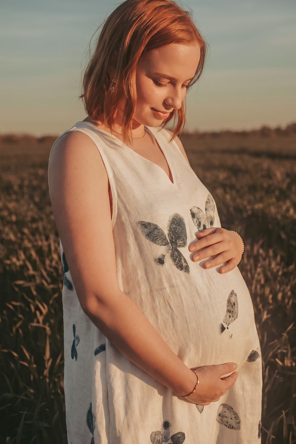 Pregnant woman wearing a hemp eco-printed dress with natural botanical leaf and flower motifs, sustainable fashion in a sunlit field