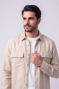 A man wearing a light beige hemp button-up shirt over a white t-shirt, standing against a light gray studio background.