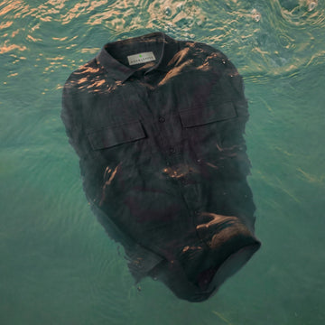 A dark gray button-up shirt with two chest pockets, floating underwater in clear turquoise water with light reflecting off the surface.