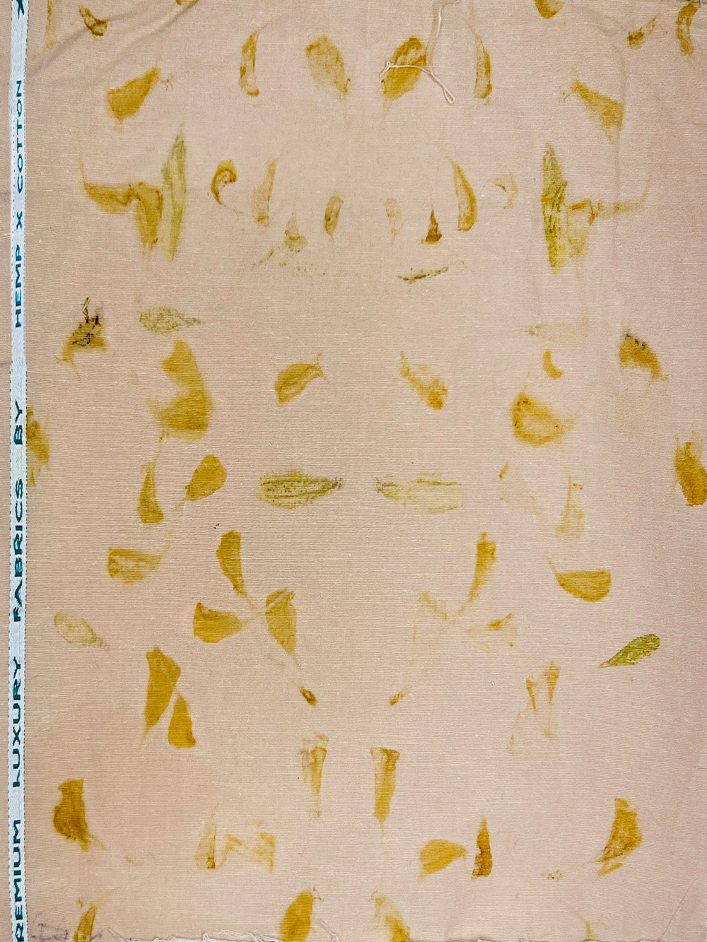 Beige hemp fabric with a scattered pattern of small yellow and olive-green botanical pieces, shown flat with a printed measurement scale on the left edge.