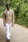A man wearing white linen trousers with a Eco_printed jacket and a white shirt, standing against a forest background.