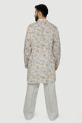 A man wearing a traditional Indian linen kurta with a mandarin collar, featuring a floral print and matching buttons, paired with light-colored trousers.
