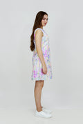 A woman standing in a studio setting, wearing a mid-length floral hemp seersucker dress with a boat neckline and sleeveless top, paired with white sneakers.