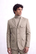 A man wearing a light beige linen-blazer with four front flap pockets over a matching beige turtleneck sweater and trousers, photographed against a plain white studio background.
