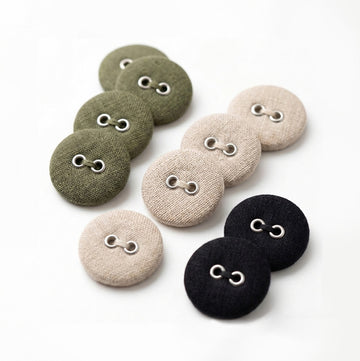 Nine round fabric-covered buttons with two metal eyelets, arranged on a white background in olive green, light beige, and black.