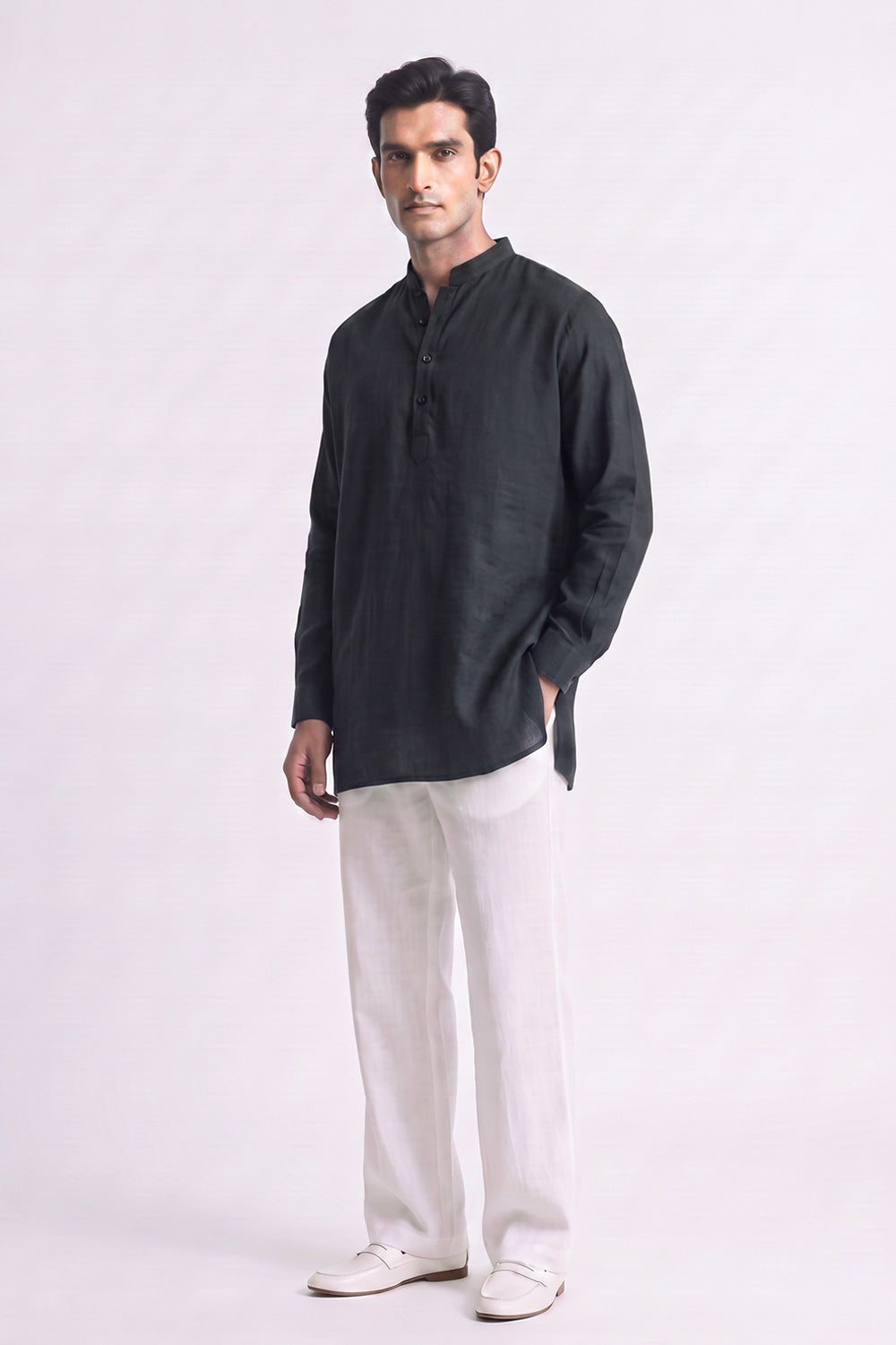 A man modeling a black long-sleeve linen kurta with a mandarin collar and white linen trousers, standing against a light gray studio background.