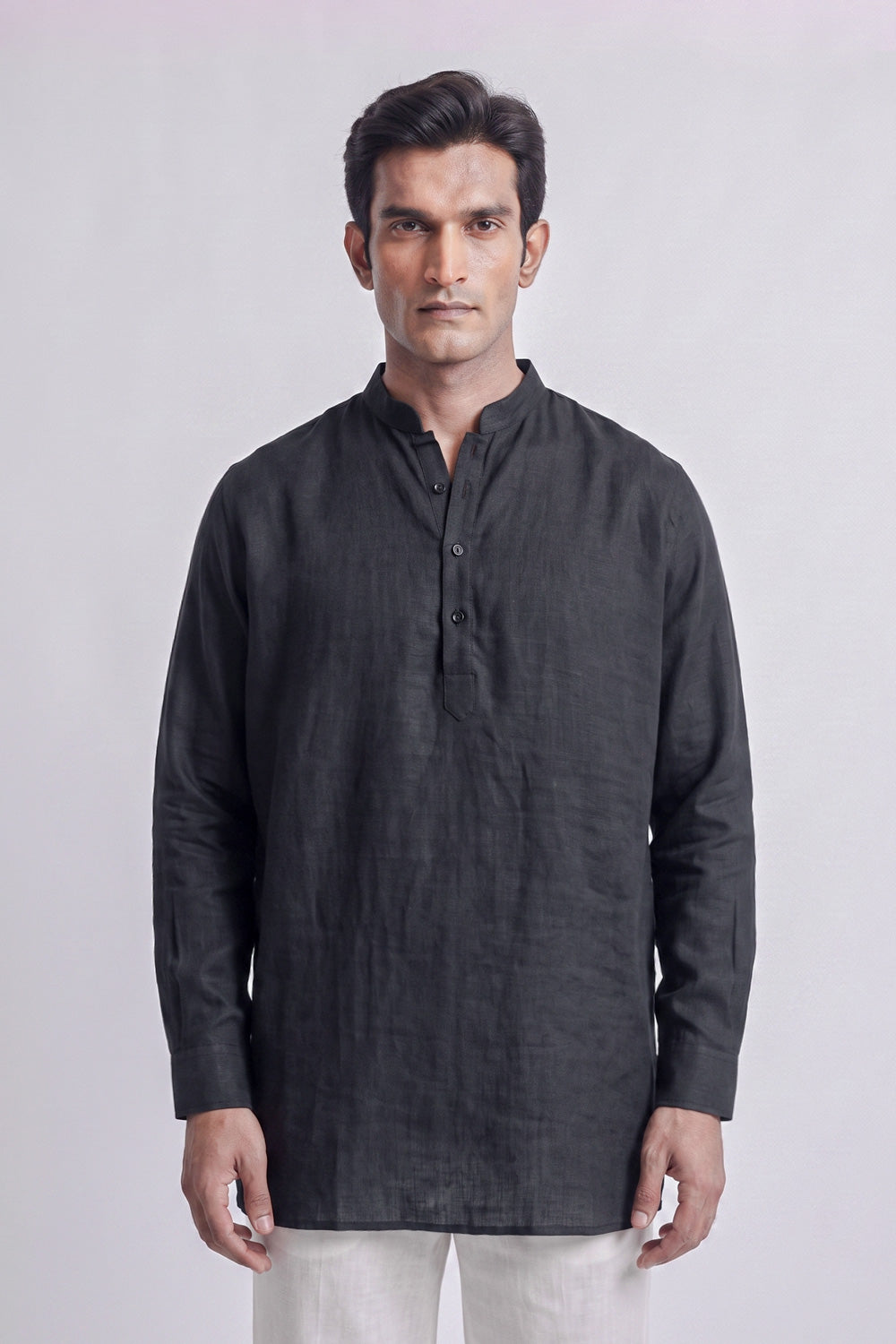 A man wearing a dark charcoal gray linen long-sleeve kurta with a mandarin collar and partial button placket, paired with off-white trousers, standing against a light gray studio background.