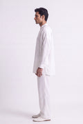 A man in a white long-sleeve linen kurta and matching trousers, standing in profile against a plain white studio background.