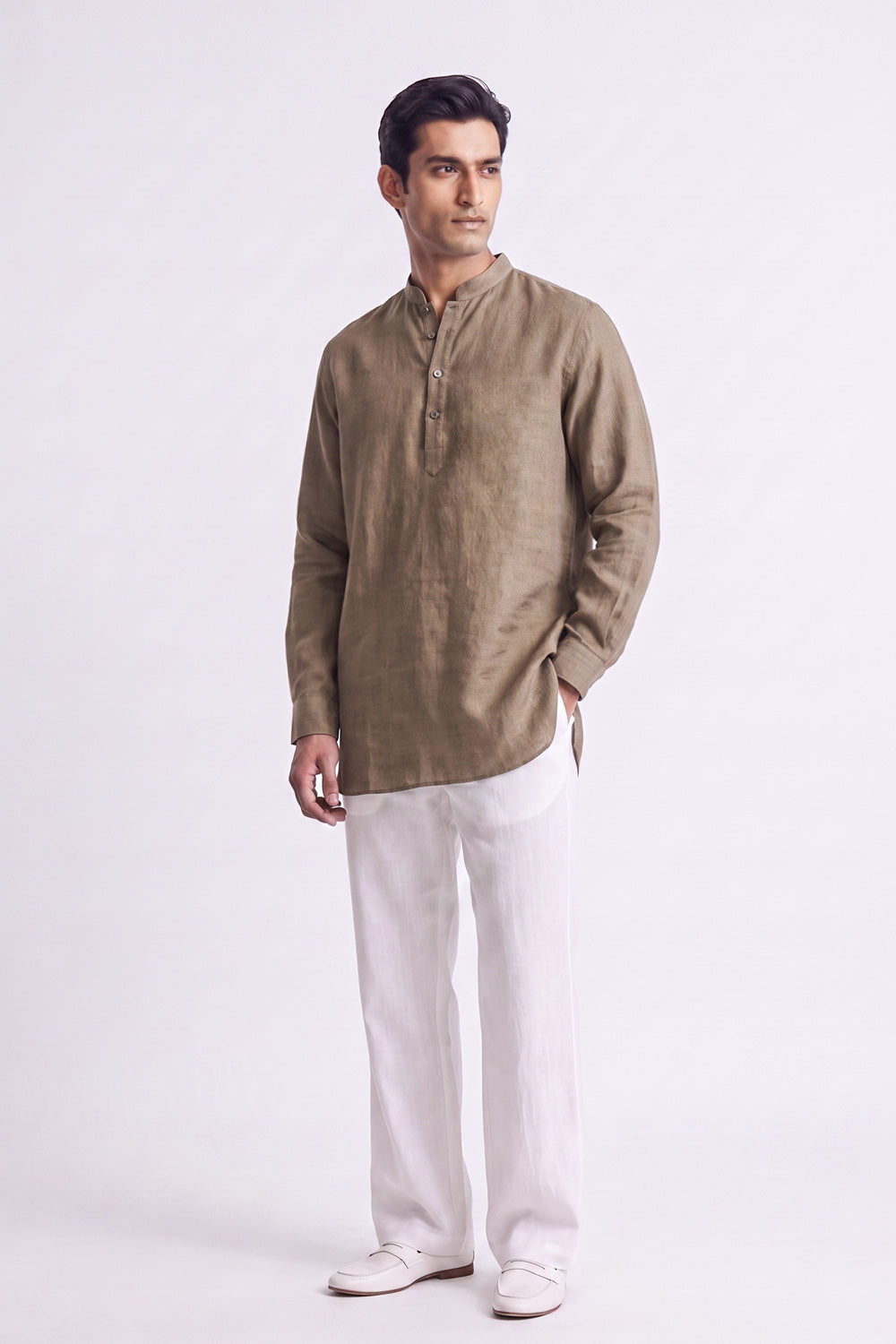 A man modeling a light brown linen long-sleeve kurta with white trousers and white shoes, standing against a plain white studio background.