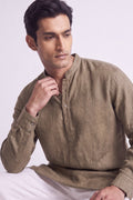A man wearing a light brown linen long-sleeve kurta with a mandarin collar and three-button placket, paired with white trousers, set against a plain light gray background.