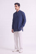 A man modeling a navy blue long-sleeve linen kurta with a mandarin collar and three-button placket, paired with off-white trousers and white shoes, against a plain light gray studio background.