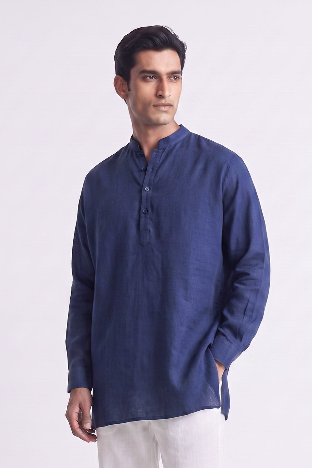 A man wearing a navy blue long-sleeve linen kurta with a mandarin collar and three-button placket, paired with white trousers, photographed against a plain white studio background.