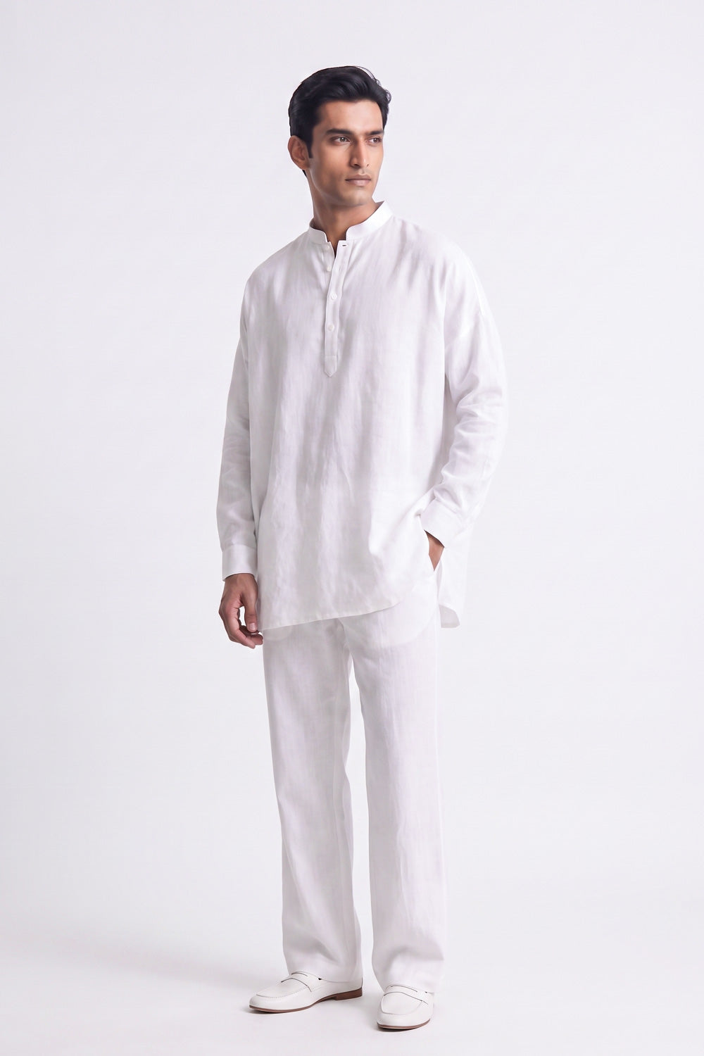 A man modeling a white long-sleeve linen kurta with a split collar and matching white trousers, standing against a plain white studio background.