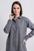 A woman modeling a long-sleeved gray linen button-up linen  shirt dress against a light gray studio background.