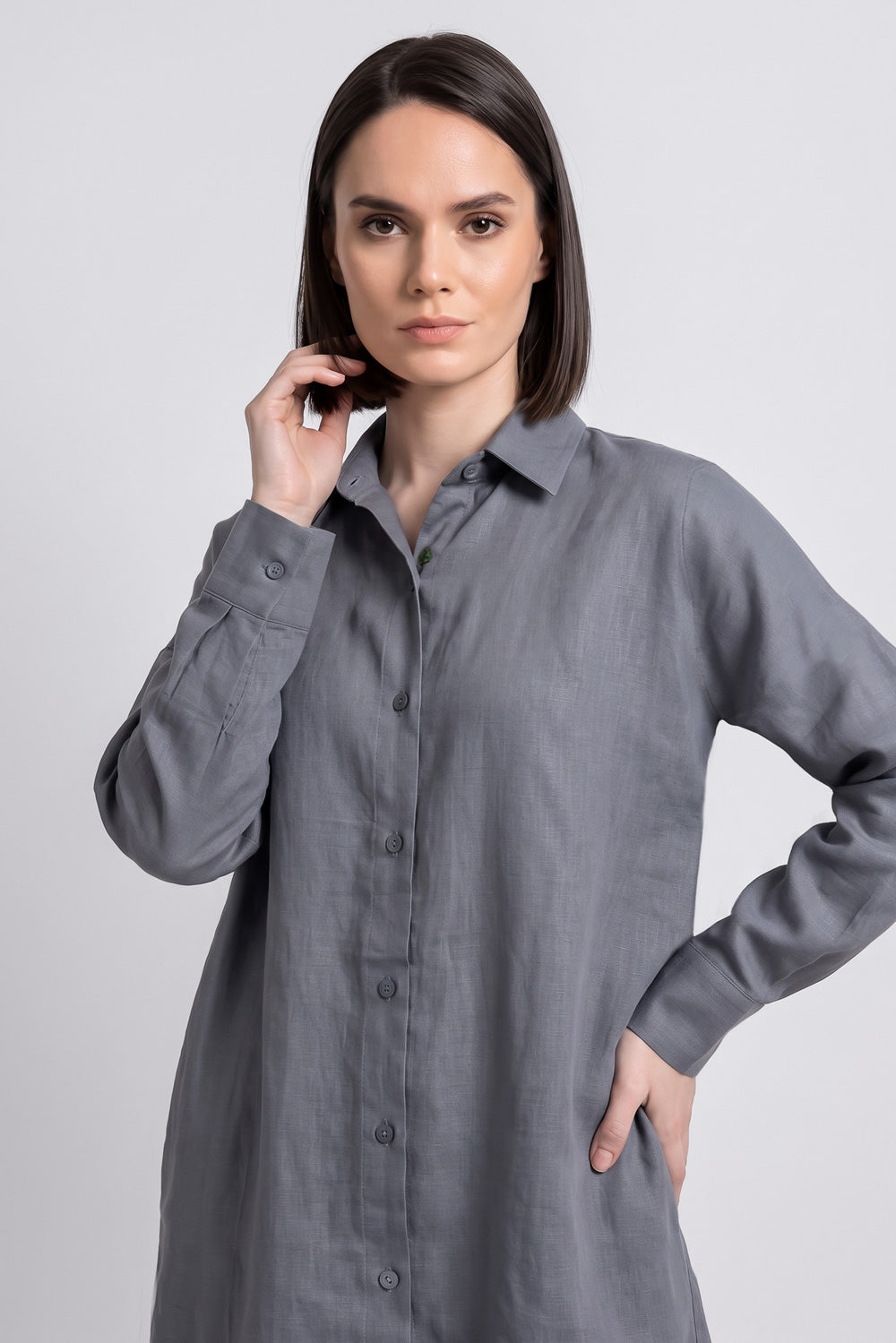 A woman modeling a long-sleeved gray linen button-up linen  shirt dress against a light gray studio background.