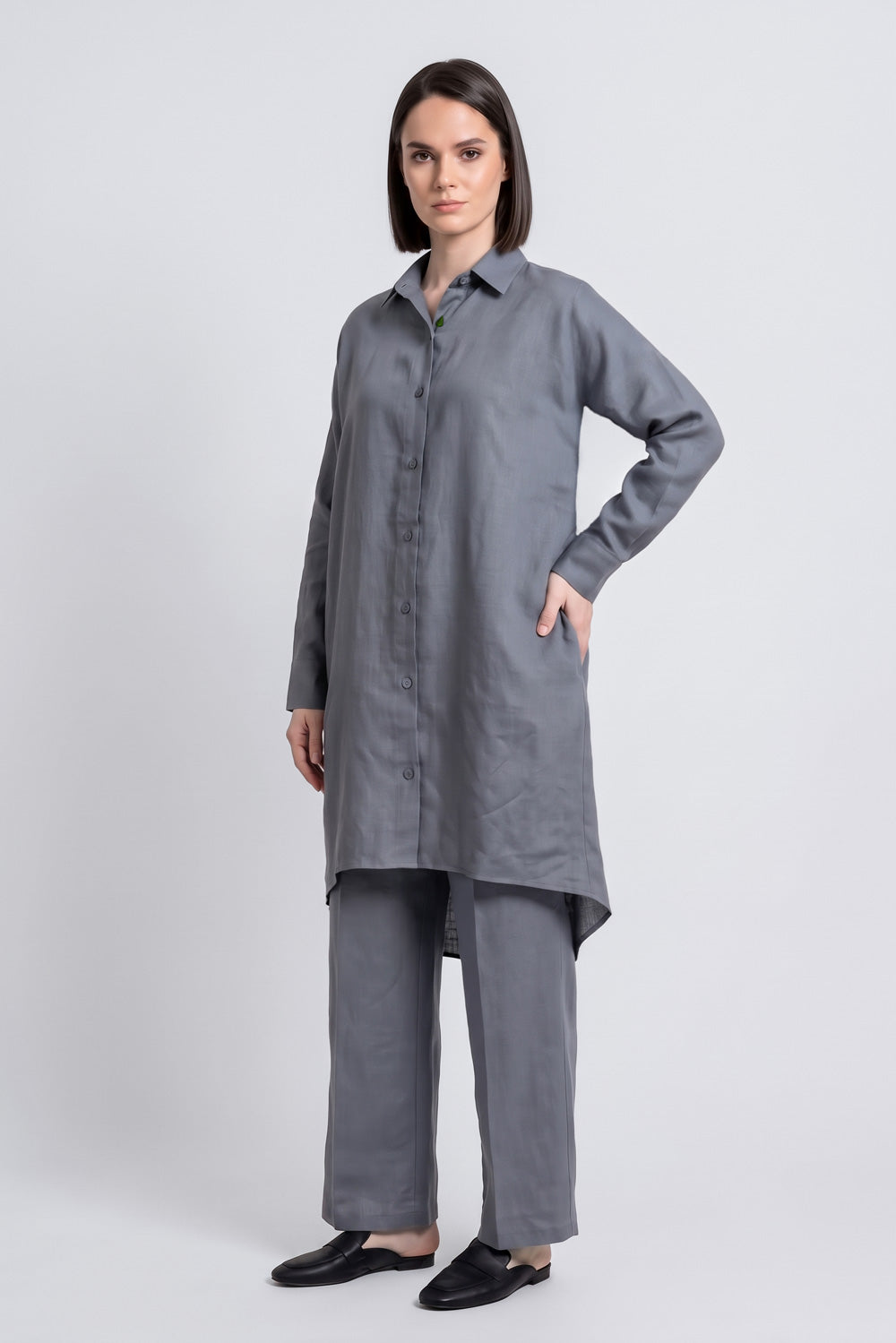 A woman modeling a long-sleeved gray button-up tunic linen  top with matching wide-leg trousers, photographed against a neutral light gray studio background.