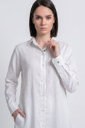 A woman modeling a white long-sleeve linen shirt with green buttons, set against a plain light gray studio background.