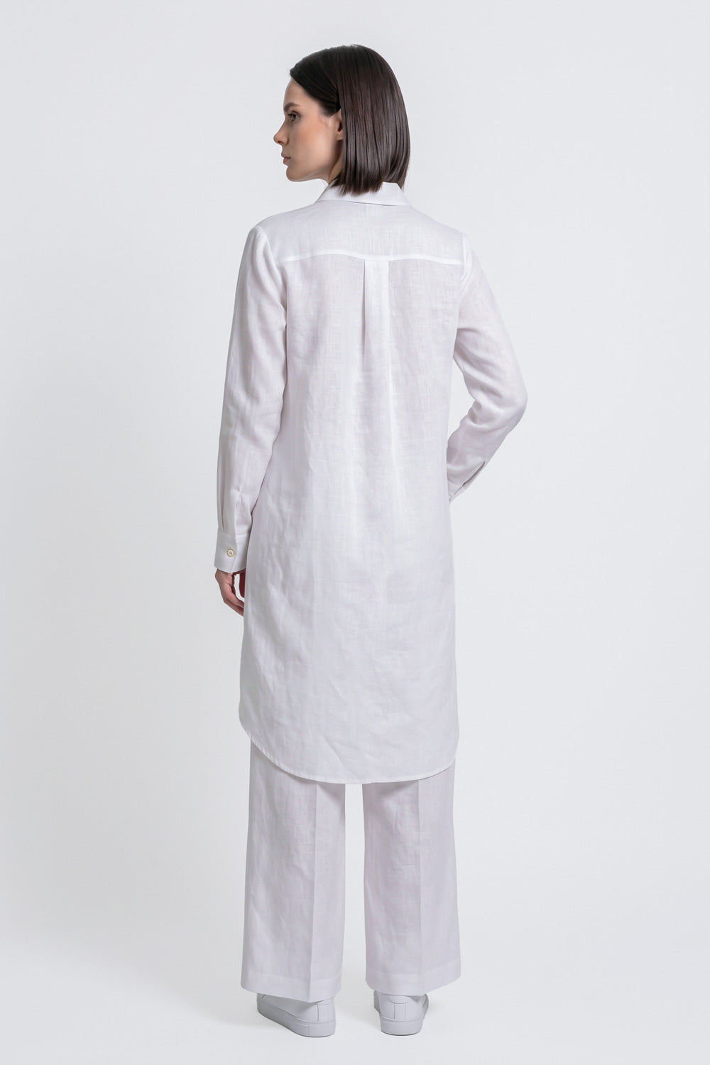 A woman shown from the back wearing a white long-sleeve linen  kurta and matching wide-leg trousers against a plain light gray studio background.