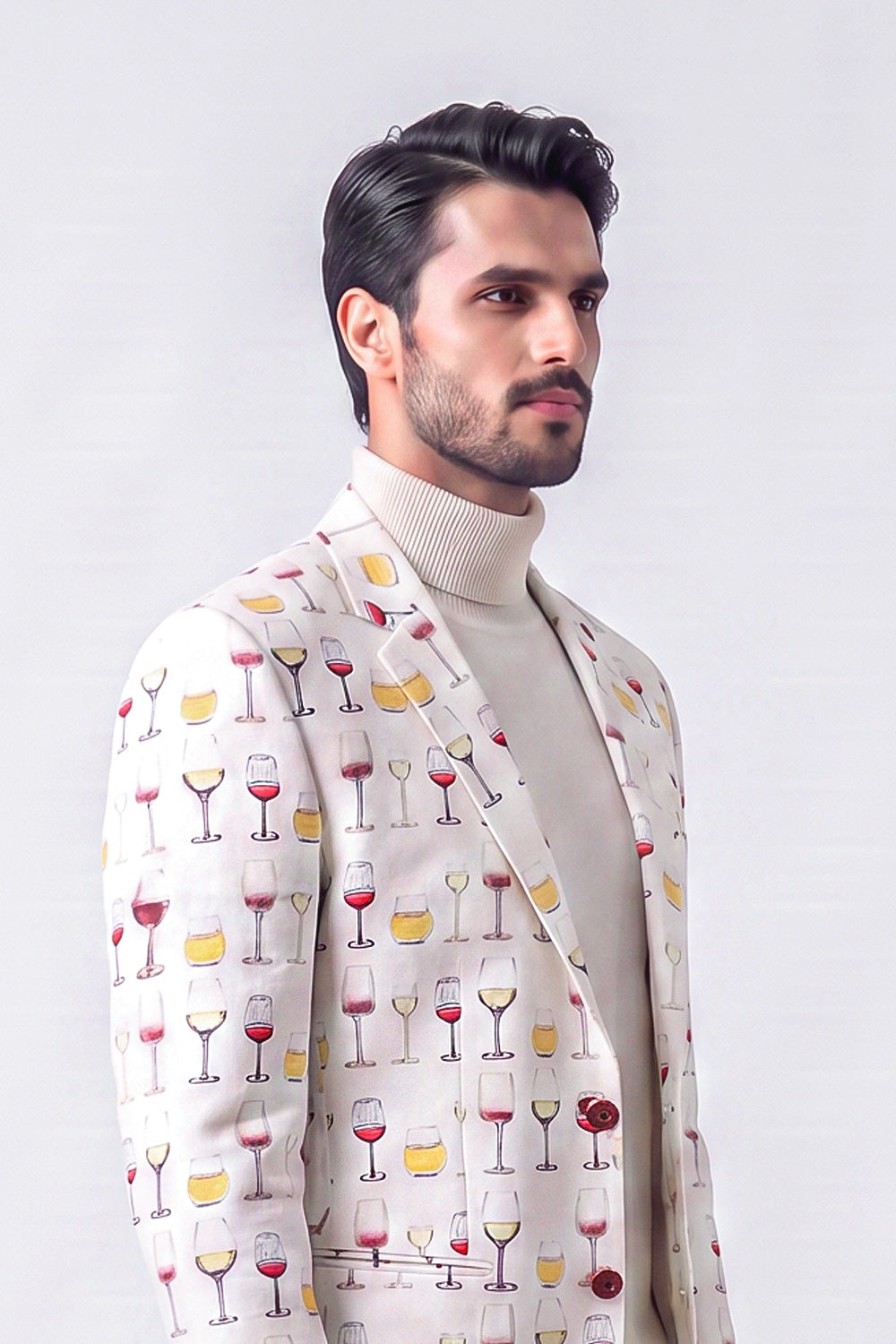 A man wearing a cream-colored blazer with a repeating pattern of wine glasses filled with red, yellow, and white liquids, layered over a beige turtleneck sweater, set against a plain light gray background.